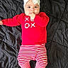 baby, infant, child, portrait, lying_down, black_blanket, red_sweater, striped_pants, white_headband, bow, clothing, indoors, bed, cute, smiling, wide_eyes, hand_to_mouth, fashion, holiday, photography