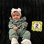 baby, infant, headband, white_shoes, green_outfit, milestone_card, 2_months, sitting, black_blanket, cute, portrait, child, smiling, indoors, plush, cozy, clothing, person, baby_girl, headwear
