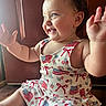 baby, child, smiling, happy, dress, american_flag, pattern, clapping, sitting, indoors, wooden_floor, face, cheeks, arms, eyes, person, cute, toddler, clothing, natural_light