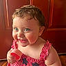 baby, child, smiling, blue_eyes, curly_hair, red_dress, checkered_pattern, holding_object, pink_cup, indoor, wooden_door, happy, cute, portrait, infant, close_up, cheerful, playful, skin, person