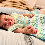 Luna is registered to the contest to win money with this photo: baby, sleeping, crochet_dress, pastel_colors, cushion, blanket, infant, peaceful, smile, soft, comfort, indoors, portrait, child, cute, relaxed, hand, face, head, cozy