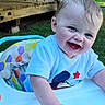 baby, child, high_chair, smiling, outdoor, grass, wooden_deck, greenery, toddler, happy, person, short_hair, blue_shirt, playful, sunlight, summer, daylight, hand, face, seat