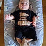 baby, black_clothing, bunny_pattern, child, cushion, cute, drool, footwear, indoor, infant, lying_down, person, plaid, relaxed, small_feet, small_hands, soft_toy, teddy_bear_design, toddler, wooden_table
