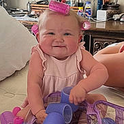 Lovelyn is registered to the contest to win money with this photo: baby, child, hair_rollers, pink, purple, smiling, indoors, bed, dresser, toiletries, cute, playing, person, infant, happy, skin, furniture, room, accessories, hair_care
