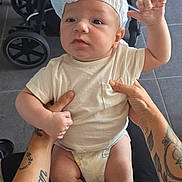 Aaron participe au concours pour gagner de l'argent avec cette photo : baby, blue, chair, curious, diaper, expression, floor, foot, hands, headwear, holding, indoor, infant, leg, person, skin, stroller, tattoo, white, white_shirt