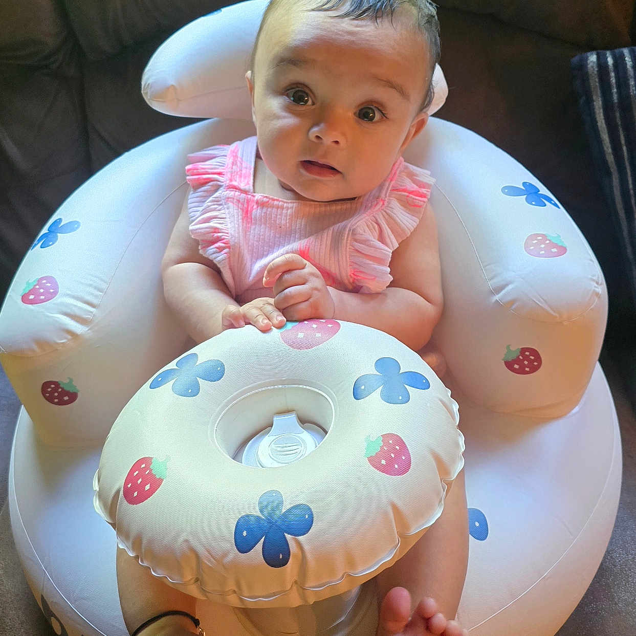 Ribha is registered to the contest to win money with this photo: baby, blue_flower_pattern, child, closeup, comfortable, couch, curious_expression, cute, face, feet, home, indoor, infant, inflatable_seat, person, pink_clothing, sitting, soft_lighting, strawberry_pattern, toes