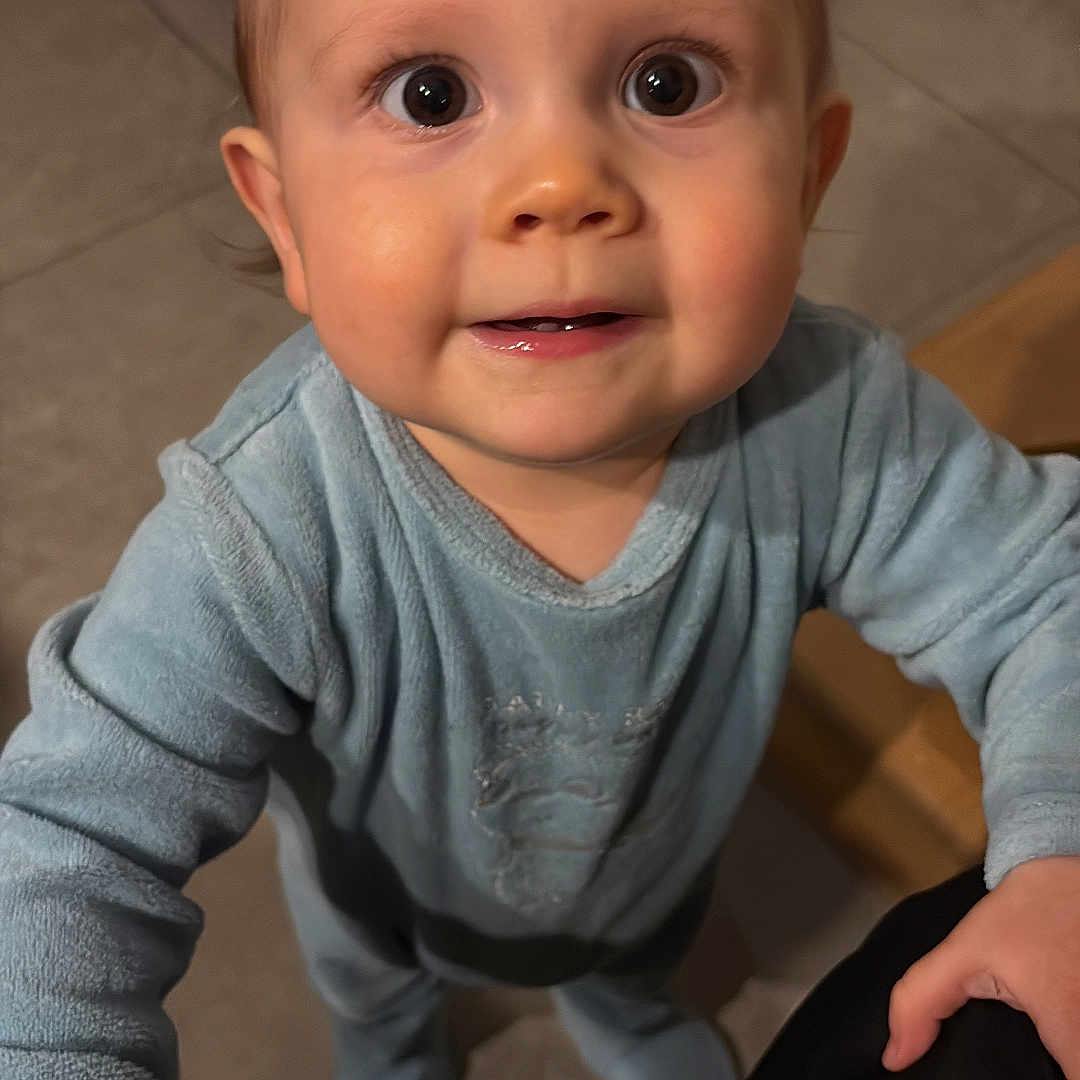 Loëvann a rejoint le concours — aidez-le/la à gagner de superbes lots ! baby, blue_clothing, child, closeup, cute, eyes, face, floor, hand, holding_hand, home, indoor, infant, pajamas, person, portrait, smile, standing, tile_floor, young_child