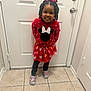 child, girl, smile, red_dress, minnie_mouse, indoor, door, tile_floor, crocs, hair_bow, curly_hair, standing, happy, casual_clothing, playful, cute, person, feet, head, fashion