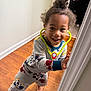Amiel is registered to the contest to win money with this photo: toddler, child, pajamas, mickey_mouse, toy_stethoscope, indoor, doorframe, wooden_floor, smiling, playful, barefoot, curly_hair, young_child, happy, person, clothing, room, home, casual, fun