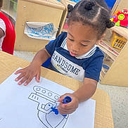 Amiel joined the competition — help win amazing prizes! child, toddler, drawing, coloring, marker, table, classroom, hair_buns, blue_marker, paper, furniture, floor, indoor, preschool, education, kid, artwork, concentration, clothing, person