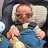 baby, sunglasses, heart_shaped, car_seat, child, toy, blanket, clothing, seatbelt, infant, cute, indoor, portrait, face, hands, pink, black, striped, comfort, relaxation