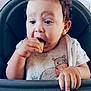 Edem a rejoint le concours — aidez-le/la à gagner de superbes lots ! baby, child, high_chair, bib, snack, food, crumbs, hand, face, mouth, curly_hair, clothing, table, indoor, portrait, cute, eating, expression, person, young