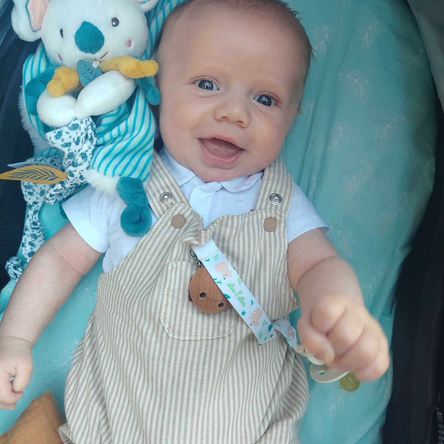 Soann a rejoint le concours — aidez-le/la à gagner de superbes lots ! baby, blue_background, button, child, closeup, cute, fabric, face, hand, happy, indoors, infant, koala, lying_down, pacifier_clip, plush_toy, smiling, soft_toy, striped_overalls, white_shirt