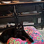 black_cat, cat, pet, indoor, cushion, embroidery, colorful, pink, yellow_tassels, feline, alert, relaxed, carpet, furniture, cabinet, television, home, animal, cute, resting