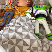 Elysio a rejoint le concours — aidez-le/la à gagner de superbes lots ! baby, blanket, couch, toy_story, woody, buzz_lightyear, toy, child, indoor, yellow_clothing, patterned_blanket, soft_fabric, relaxed, lying_down, plush_toy, face, person, furniture, comfort, nap_time