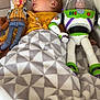 baby, blanket, couch, toy_story, woody, buzz_lightyear, toy, child, indoor, yellow_clothing, patterned_blanket, soft_fabric, relaxed, lying_down, plush_toy, face, person, furniture, comfort, nap_time