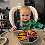 Lennox is registered to the contest to win money with this photo: baby, infant, high_chair, feeding_tray, plate, strawberries, blueberries, finger_food, smiling, happy, harness, onesie, striped_clothing, blonde_hair, blue_eyes, meal, kitchen, bookshelf, indoor, toddler