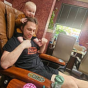 Lennox is registered to the contest to win money with this photo: adult_male, child, family_moment, hair, infant, interior, leather_chair, man, parenting, pedicure_spa, pink_toy, plant, playful, relaxed, remote_control, salon_chair, sippy_cup, smile, toys, window