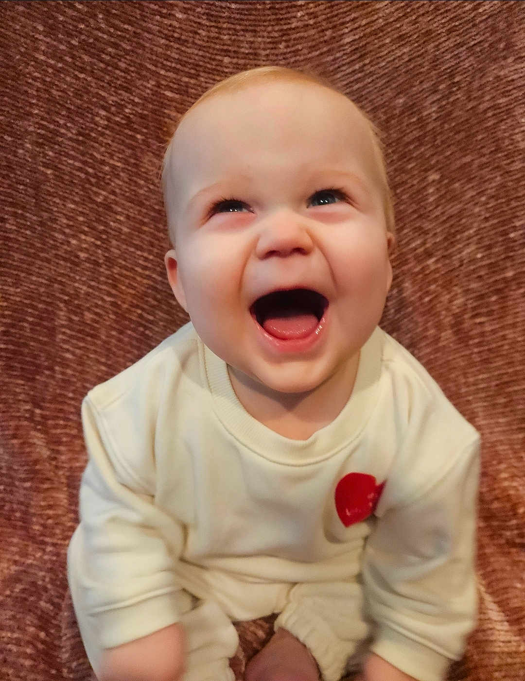 Lennox joined the competition — help win amazing prizes! baby, infant, laughing, smiling, portrait, close_up, cute, cheerful, cream_outfit, sweatshirt, seated, indoor, blanket, textured_background, face, eyes, mouth, tongue, hands, happy