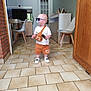 Milan a rejoint le concours — aidez-le/la à gagner de superbes lots ! toddler, child, indoor, kitchen, floor_tiles, white_shirt, orange_shorts, sunglasses, pacifier, bag, remote_control, shoes, chair, cabinet, door, clock, person, standing, modern_interior, home