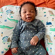 Kalvary joined the competition — help win amazing prizes! baby, smiling, onesie, stars, pillow, dinosaur_pattern, curly_hair, infant, orange_blanket, cute, happy, lying_down, child, sleepwear, relaxed, indoors, portrait, small_hand, cozy, soft