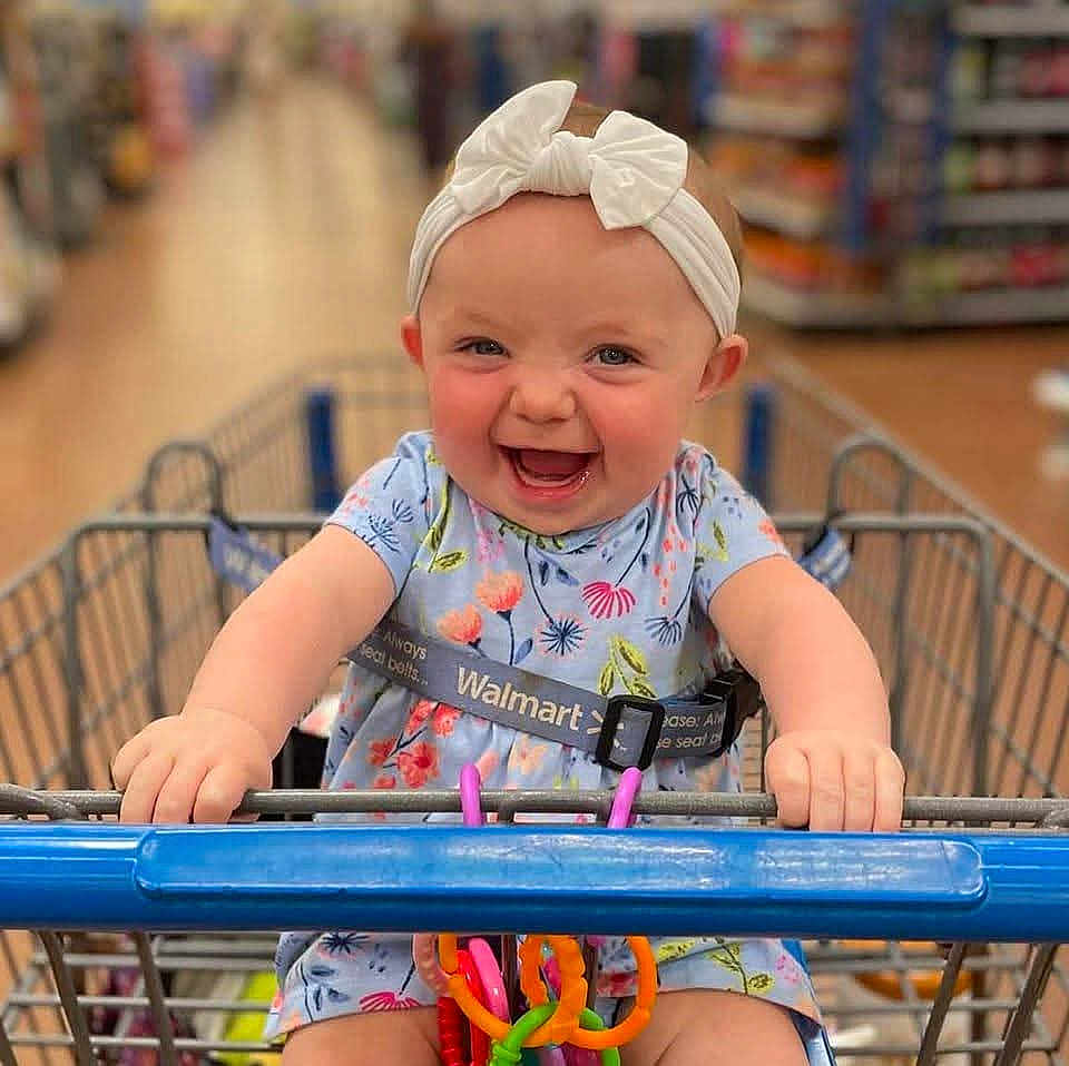 Angel is registered to the contest to win money with this photo: baby, child, shopping_cart, walmart, headband, bow, dress, smile, happy, toy, colorful, aisle, store, retail, infant, grip, cute, person, seatbelt, shopping