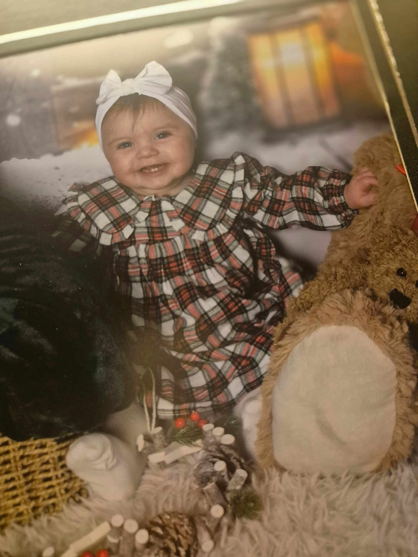 Mylah is registered to the contest to win money with this photo: baby, child, plaid_dress, headband, smiling, teddy_bear, blanket, holiday_decorations, pine_cones, basket, soft_toys, festive, indoor, portrait, cute, happy, cozy, winter_theme, childrens_clothing, sitting