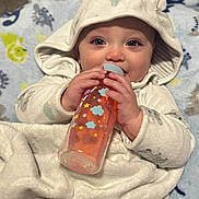 Waylon is registered to the contest to win money with this photo: baby, bottle, blanket, hood, infant, cute, smiling, blue_eyes, hand, face, clothing, cozy, child, indoors, soft_texture, patterned_blanket, warm, lying_down, adorable, feeding