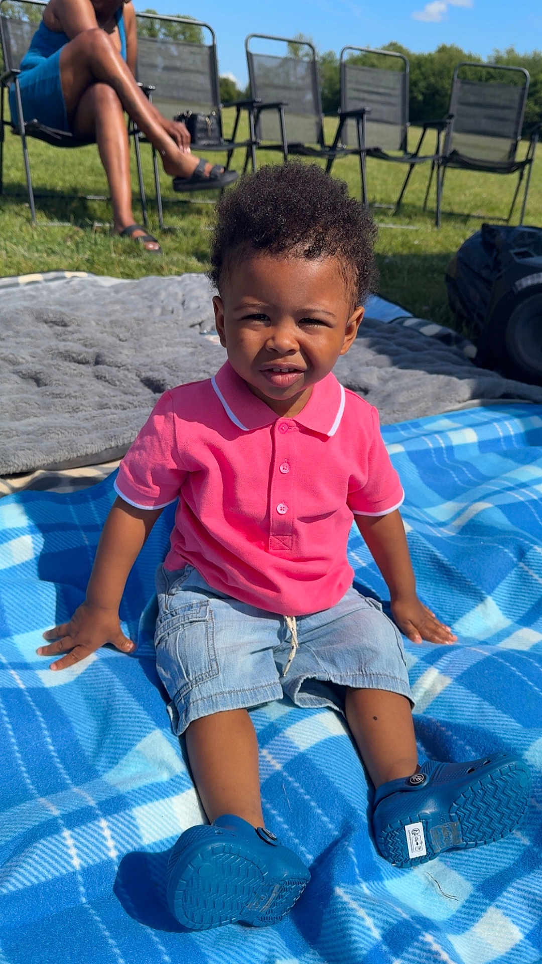 Kordero joined the competition — help win amazing prizes! toddler, child, boy, outdoor, blanket, blue, pink_shirt, denim_shorts, grass, sunlight, shoes, person, sitting, summer, casual_clothing, portrait, expression, nature, chair, relaxation