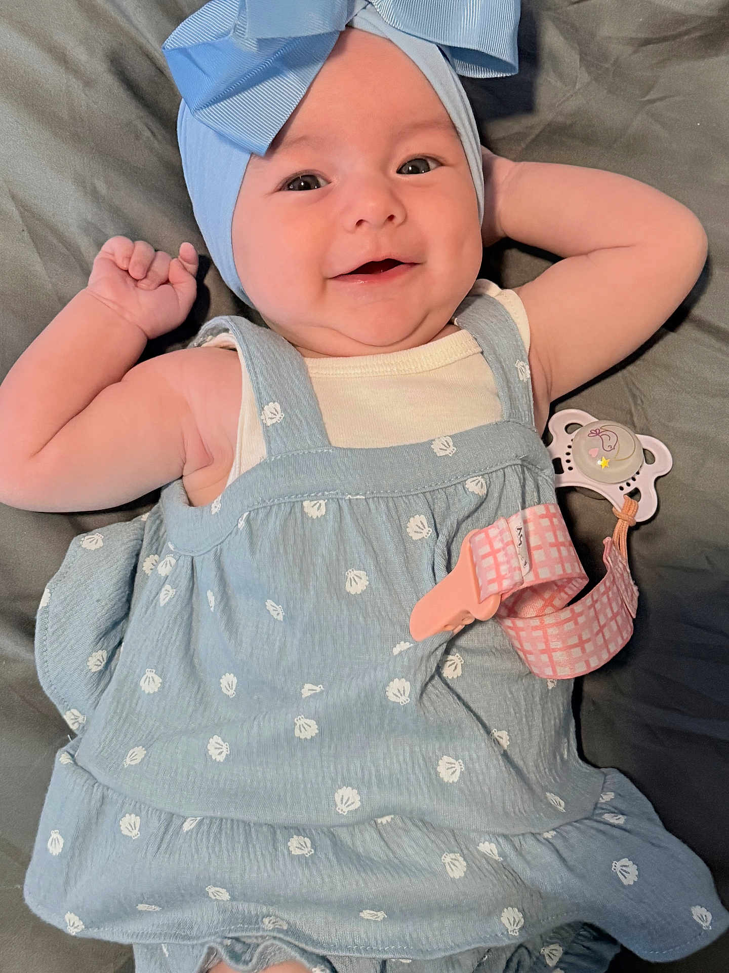 Salem joined the competition — help win amazing prizes! baby, child, smile, blue_bow, dress, lying_down, pacifier_clip, infant, cute, happy, face, skin, arm, hand, blanket, indoors, portrait, wearing, headwear, clothing