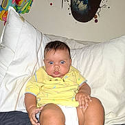 Marcus joined the competition — help win amazing prizes! baby, diaper, yellow_shirt, pillow, bed, stuffed_animal, toy, indoor, child, curious, wide_eyes, sitting, person, face, skin, hand, foot, sock, wall_art, blanket