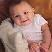 Myles is registered to the contest to win money with this photo: baby, brown_leather, child, couch, cozy, cute, face, foot, hand, happy, home, indoors, infant, pillow, portrait, sitting, skin, smile, white_onesie, young