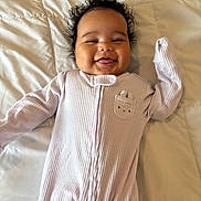 Lailani Jackson joined the competition — help win amazing prizes! baby, bed, cheeky, child, cozy, curly_hair, cute, cute_expression, happy, indoor, infant, lying_down, onesie, portrait, purple_clothing, quilt, smiling, soft_lighting, tongue_out, young_child