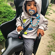 Mylan participe au concours pour gagner de l'argent avec cette photo : toddler, child, pacifier, hoodie, bike_seat, bicycle, outdoor, greenery, pathway, mickey_mouse, clip, casual_clothing, socks, curious, holding, black, seatbelt, sitting, young_child, baby