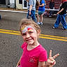 Harley joined the competition — help win amazing prizes! child, girl, face_paint, peace_sign, pink_shirt, umbrella, street, people, walking, tent, american_flag, casual_clothing, outdoor, daytime, smiling, happy, event, public_space, sidewalk, background