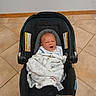 baby, blanket, car_seat, infant, floor, tile, expression, face, person, indoors, seat, cozy, wrapped, cute, newborn, child, home, furniture, carrying_device, portrait