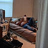 man, baby, bed, room, window, blinds, pillow, jeans, shirtless, carseat, hat, floor, clutter, door, blanket, cradle, casual, indoor, parenting, relaxing