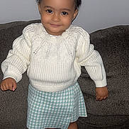 Priseis joined the competition — help win amazing prizes! toddler, child, smiling, curly_hair, white_sweater, blue_skirt, standing, couch, indoors, cute, happy, face, person, fashion, knitted, socks, white_socks, portrait, young_child, cozy