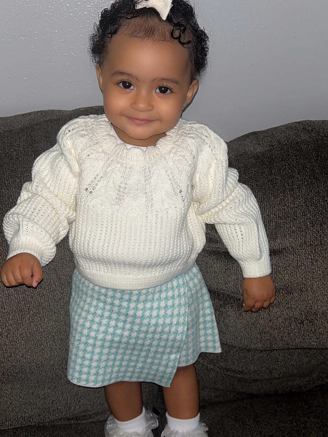 Priseis joined the competition — help win amazing prizes! toddler, child, smiling, curly_hair, white_sweater, blue_skirt, standing, couch, indoors, cute, happy, face, person, fashion, knitted, socks, white_socks, portrait, young_child, cozy