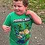 child, curly_hair, green_tshirt, minecraft, outdoor, park, pathway, grass, leaves, pumpkin, smiling, boy, casual_clothing, nature, daylight, person, short_sleeve, cute, happy, playful