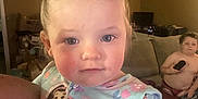 Olivia is registered to the contest to win money with this photo: toddler, child, pigtails, pajamas, cartoon, person, indoor, living_room, sofa, remote_control, shirtless, couch, adult_arm, rosy_cheeks, young_child, home, furniture, cute, portrait, family