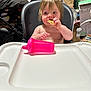 toddler, child, high_chair, snack, pink_sippy_cup, indoor, babytrend, eating, cute, messy_background, wooden_floor, plastic_tray, person, young_child, feeding_time, casual, home, curly_hair, blue_eyes, bare_chest