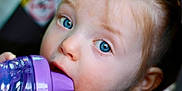 Olivia is registered to the contest to win money with this photo: baby, blue_eyes, child, closeup, curiosity, drinking, expression, face, hair, hand, indoor, innocence, mouth, person, portrait, purple, sippy_cup, skin, toddler, young_child