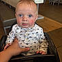 baby, child, high_chair, indoor, blue_eyes, hand, white_shirt, patterned_clothing, curious, rosy_cheeks, seated, person, furniture, table, floor, light, skin, young_child, cute, expression