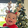 baby, child, smiling, reindeer_antlers, christmas_tree, holiday, festive, red_sweater, indoor, happy, face, person, decoration, seasonal, celebration, cute, headband, greenery, ornaments, joy