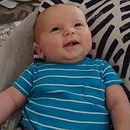 Jace is registered to the contest to win money with this photo: baby, infant, blue_onesie, striped_clothing, smiling, face, head, legs, cushion, patterned_cushion, indoor, floor, wooden_floor, shoes, black_shoes, happy, child, person, seated, home