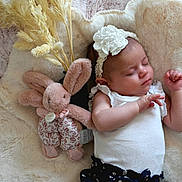 Joey a rejoint le concours — aidez-le/la à gagner de superbes lots ! baby, sleeping, plush_toy, headband, flower, blanket, soft_toy, pampas_grass, infant, cute, child, white_top, floral_skirt, resting, cozy, indoor, peaceful, adorable, skin, person
