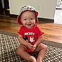 Karson is registered to the contest to win money with this photo: baby, child, smiling, sitting, indoor, red_clothing, hat, mickey_mouse, flooring, carpet, pattern, happy, person, infant, cute, toddler, onesie, headwear, room, wall