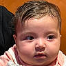 Yasmin joined the competition — help win amazing prizes! baby, infant, child, portrait, face, wide_eyes, brown_hair, pink_clothing, rosy_cheeks, looking_at_camera, indoor, close_up, seated, cushioned_seat, brown_background, head, eyes, nose, mouth, photography