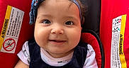 Yasmin is registered to the contest to win money with this photo: baby, infant, child, smiling, portrait, headband, bow, car_seat, red, black, sitting, indoors, face, eyes, hands, clothing, dress, safety_label, close_up, happy